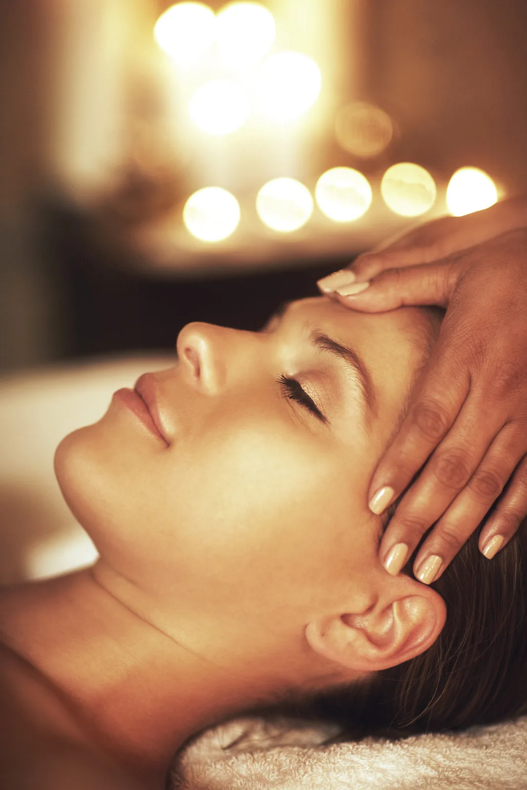 Calm woman in candlelight with hands resting on her forehead during a Reiki session