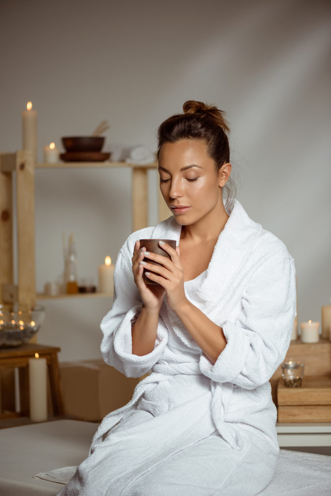 A guest in a robe enjoying a warm drink in a candlelit spa